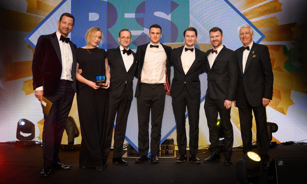 six men and one woman in black-tie attire posing with an award