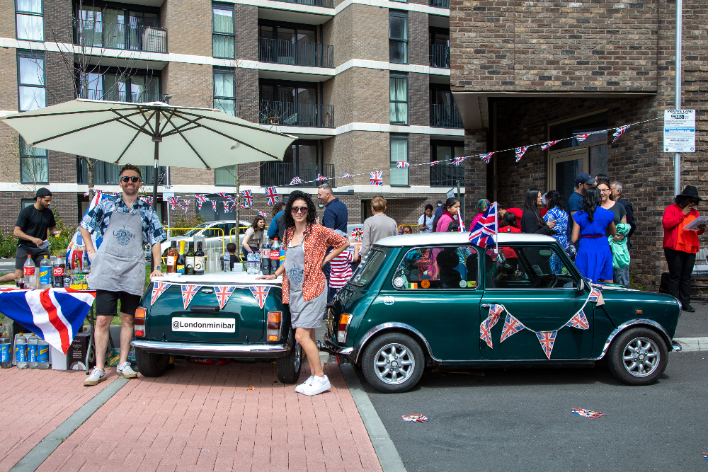 A man and a woman pose in front of a green Mini car covered in Union Flag bunting